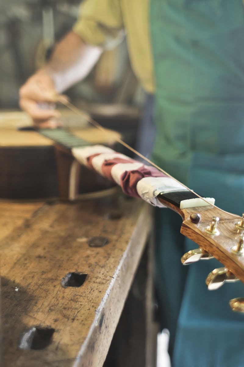 A skilled craftsman works on a guitar in a traditional workshop setting, focusing on details.